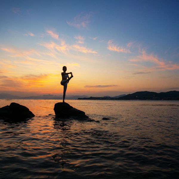 Silhouette of a person in a yoga balance pose against a sunset.